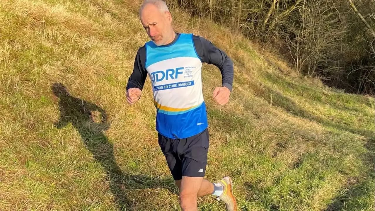 A runner in a diabetes charity vest mid-stride on a grassy hillside