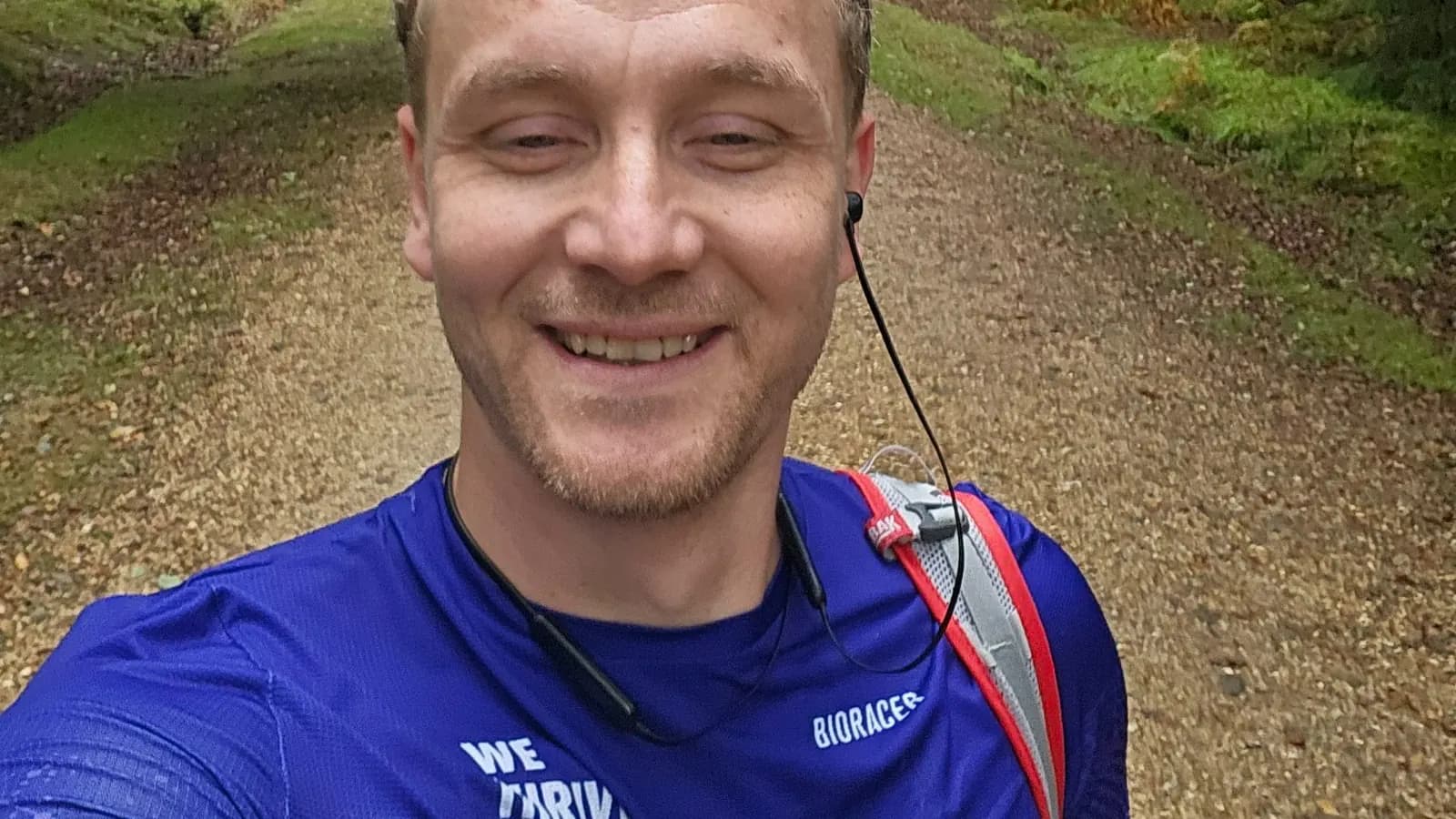 A runner smiling on a forest trail mid-marathon, wearing a shirt reading we thrive with diabetes
