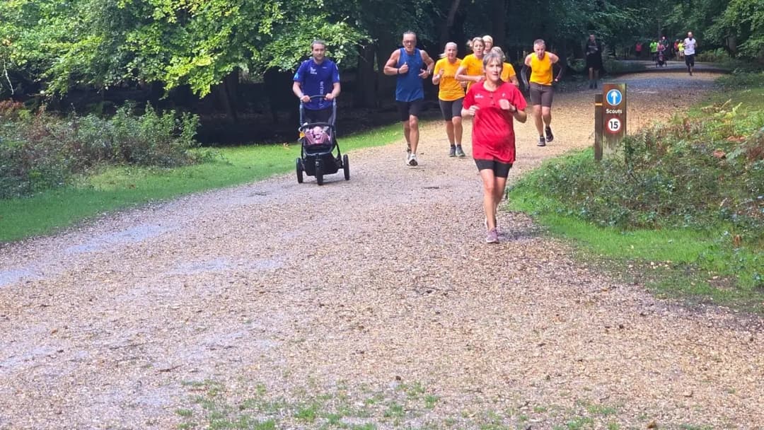 A group of runners of mixed ages coming down a gravel forest track at a parkrun, one pushing a buggy