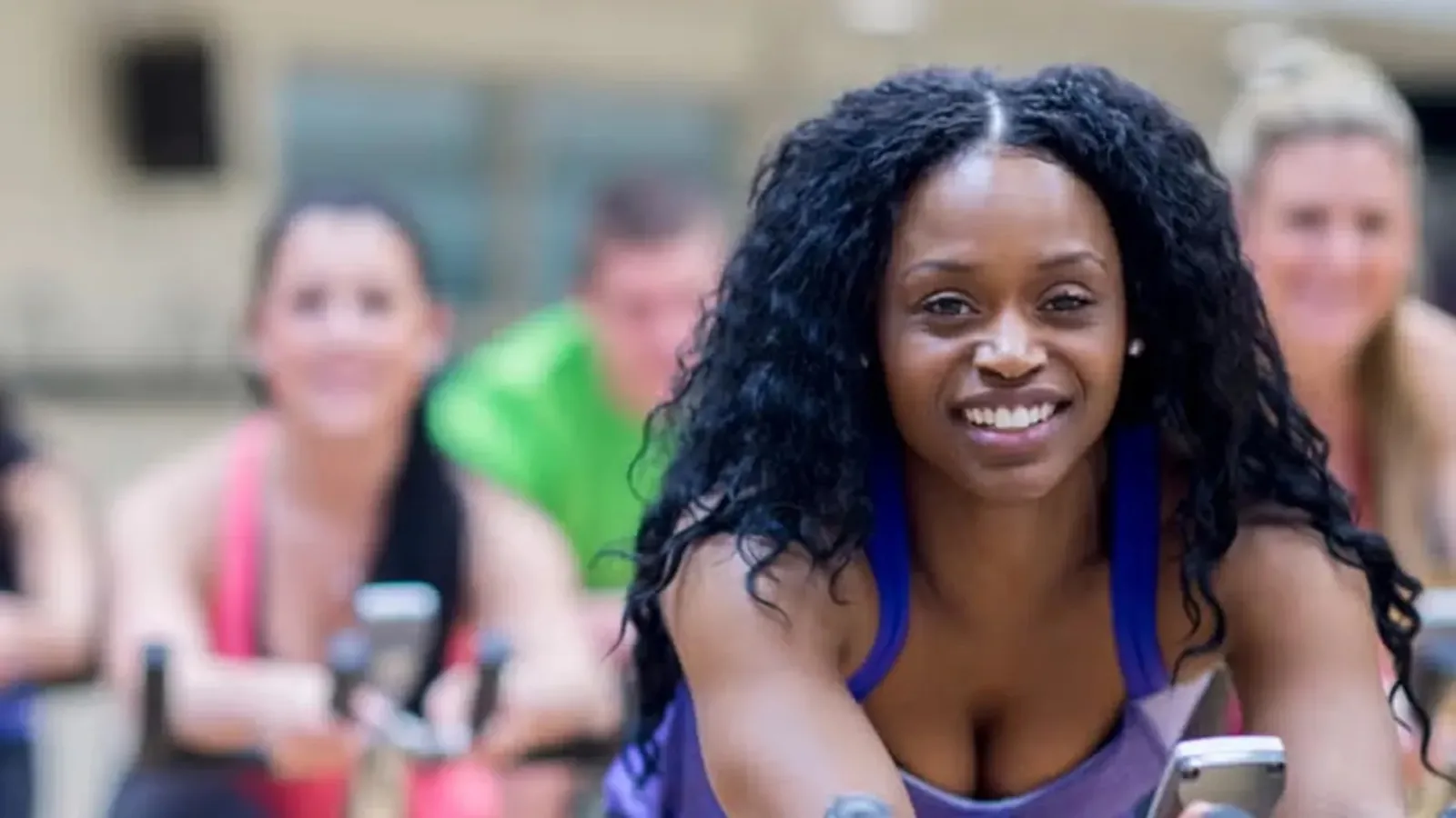 A smiling participant on an indoor cycling bike during a group class